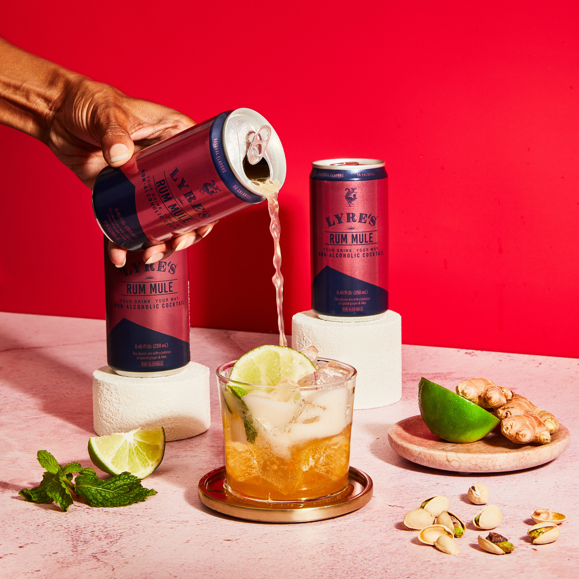 Hand pouring Lyre's non alcoholic Rum Mule into a glass with lime, mint and ginger garnish.