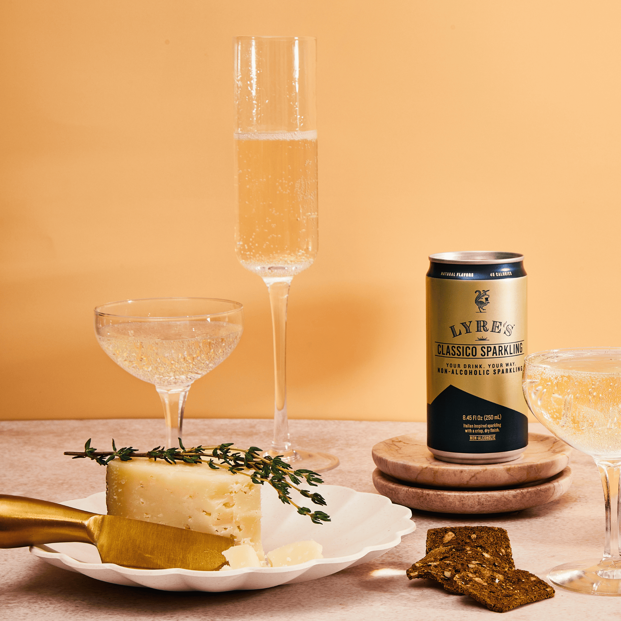Cheese platter with Lyres' non alcoholic sparkling wine can, glasses, and crackers on a table.