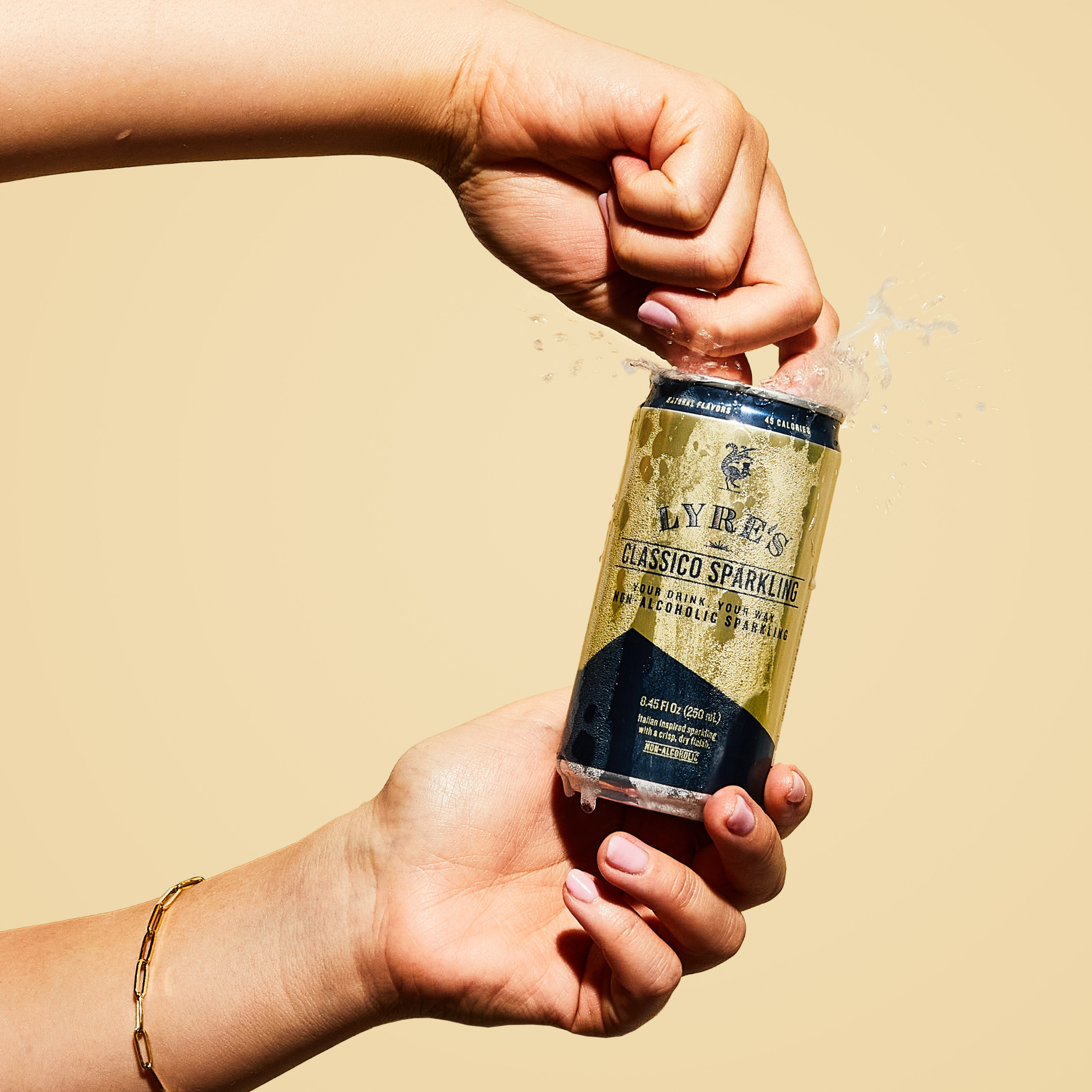 Hand holding a bottle of Lyres Classico Sparkling non alcoholic cocktail against a beige background