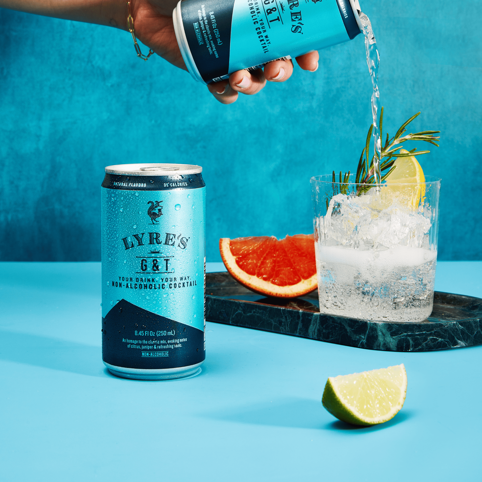 Lyre's non-alcoholic G&T being poured into a glass with ice and a slice of lemon on a blue background.