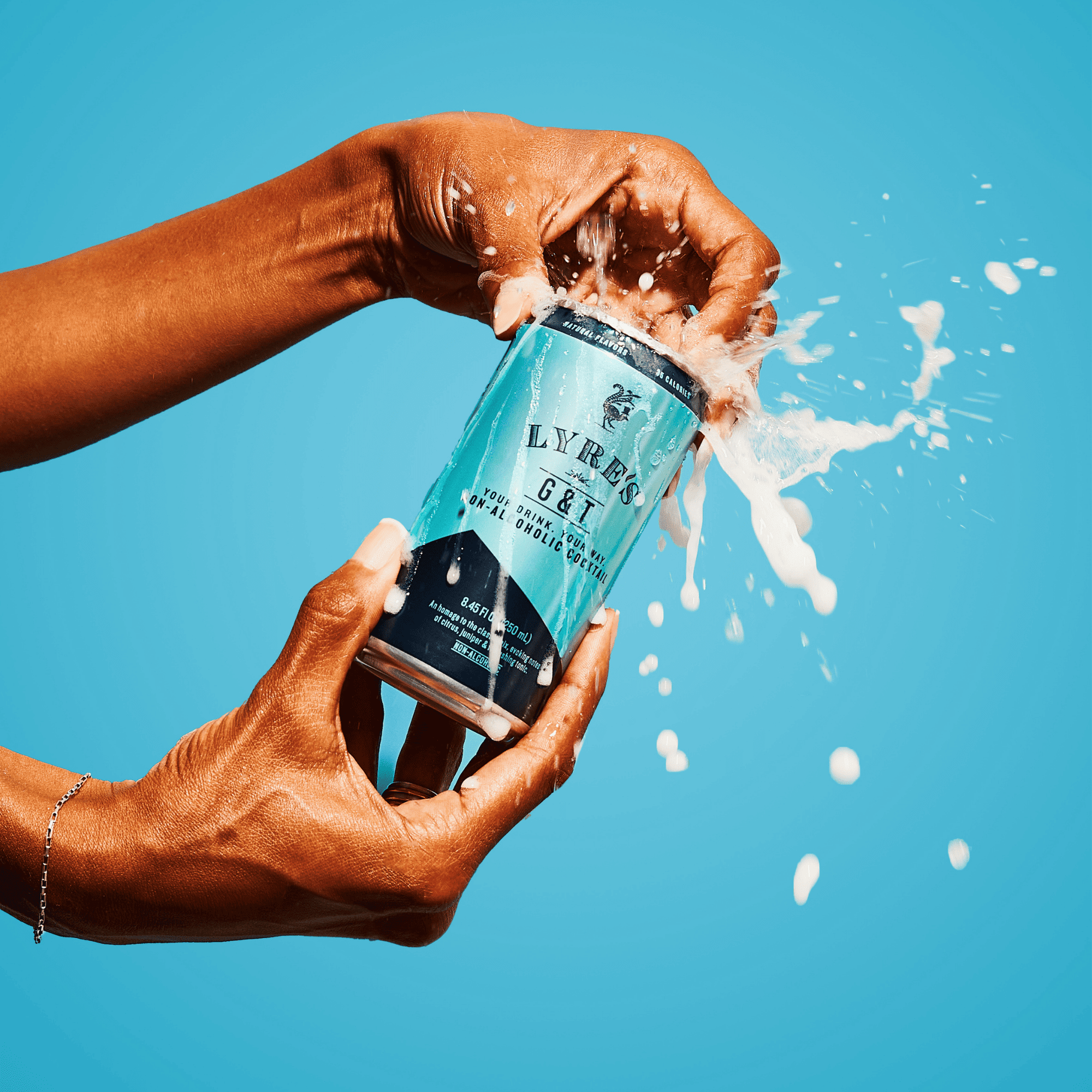 Person opening a can of Lyre's non alcoholic Gin and Tonic with a blue background