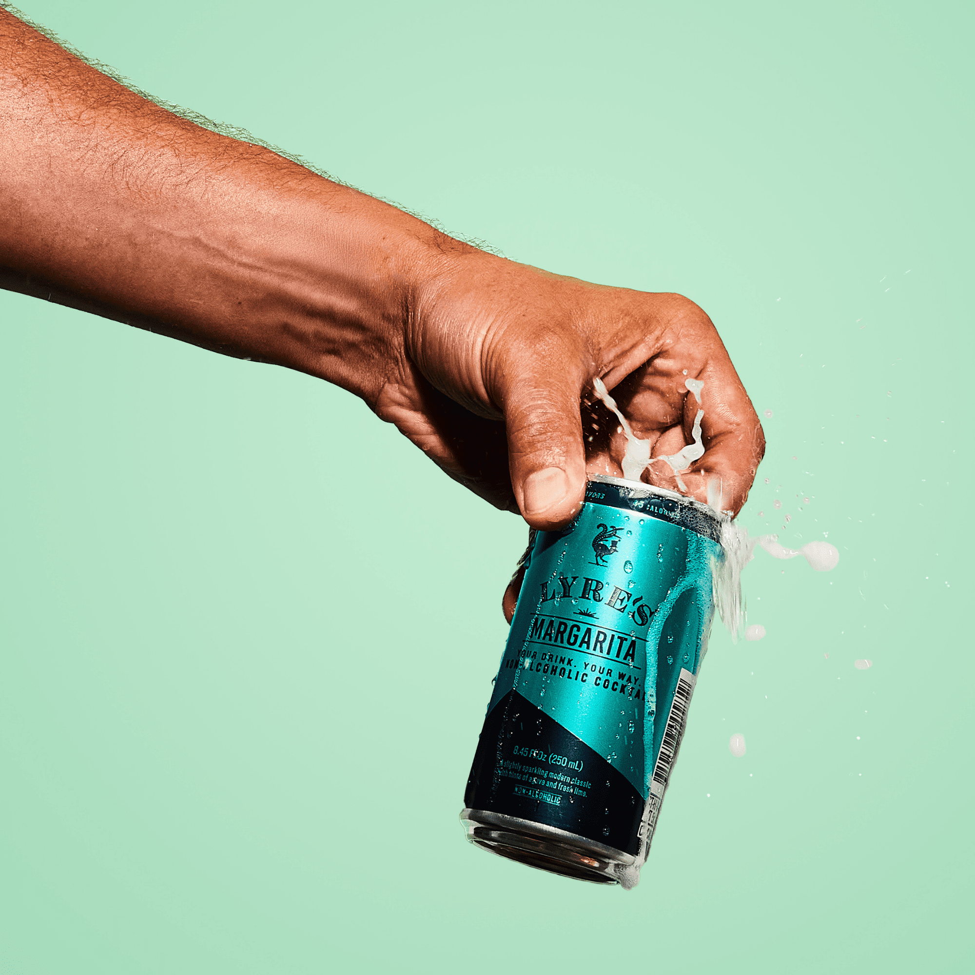 Hand opening a can of Lyre's Non Alcoholic Margarita against a light green background