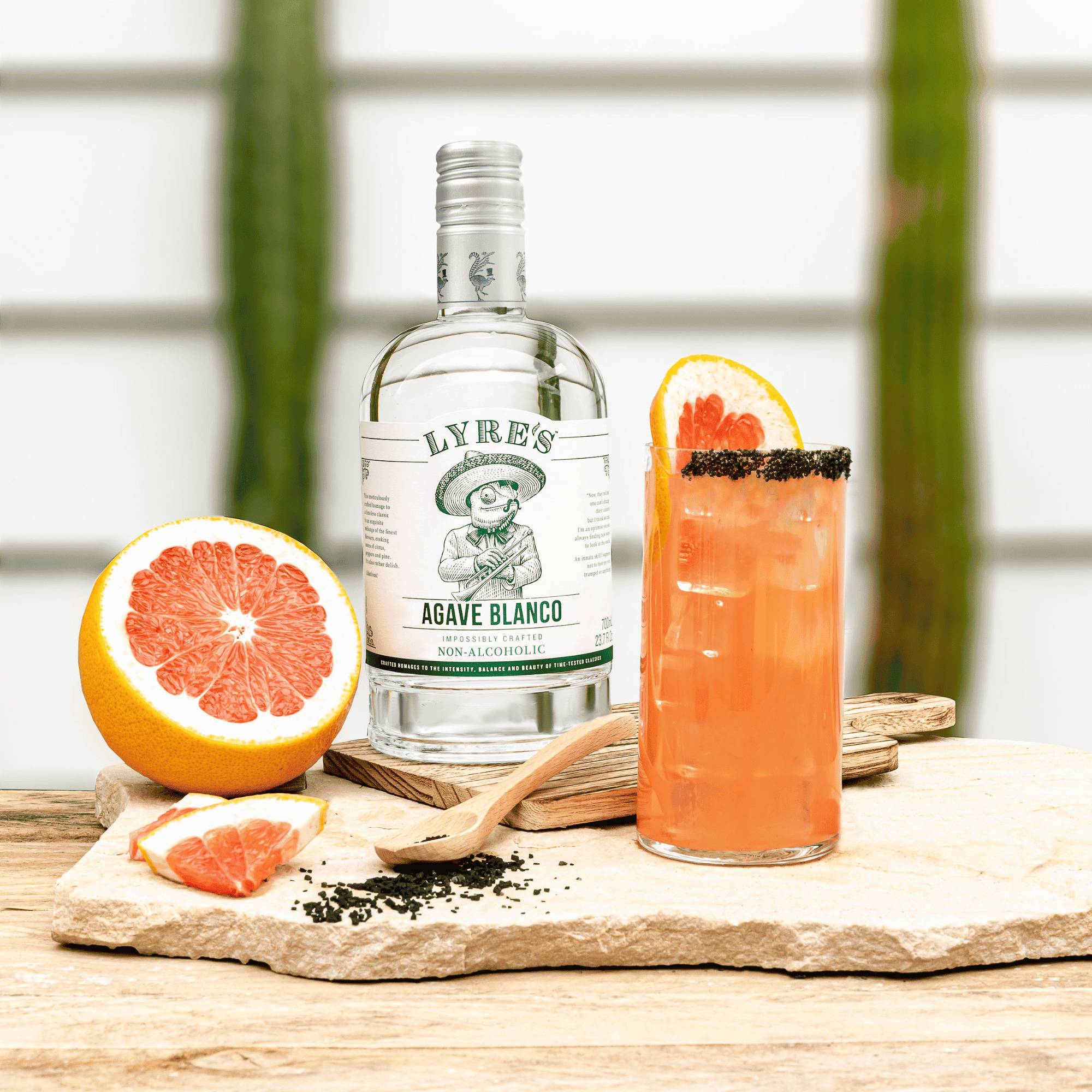 Bottle of Lyres Agave Blanco with a non-alcoholic Paloma and grapefruit on a wooden surface.