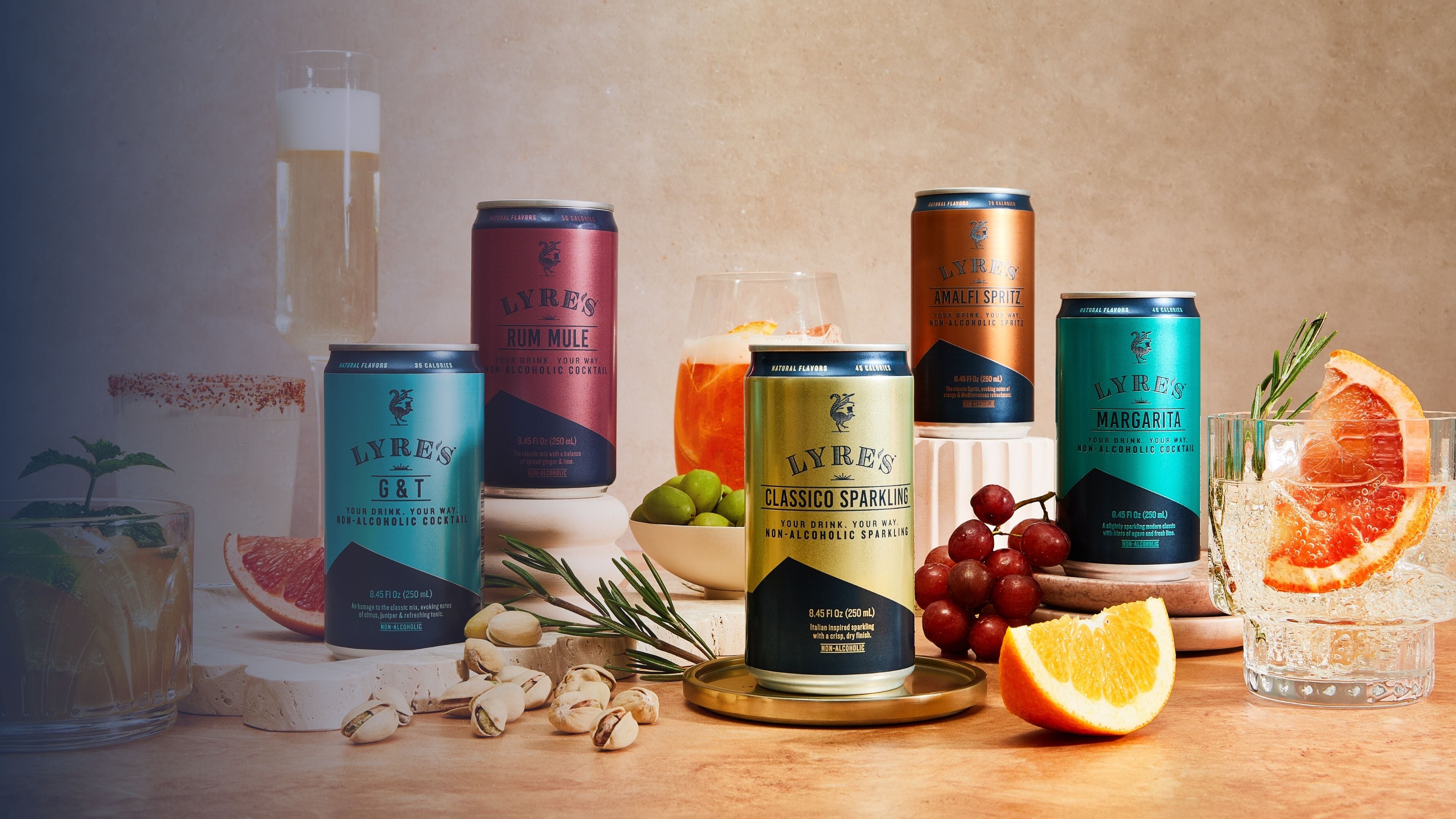 Cans of Lyre's non alcoholic cocktails in a can on a table with grapes, oranges, and cocktails.
